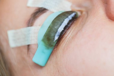 Bir kadının yüzünde kirpik kaplama prosedürü. Bir kozmetolog, kirpik uzatma işlemi sırasında bir kadının gözüne cımbızla uzun kirpikleri yapıştırır..