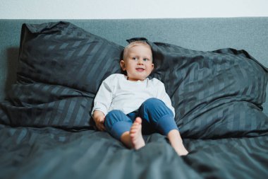 Pijama giyen, dinlenen ve yatakta oynayan 2 yaşında komik bir çocuk. Küçük çocuk yatakta oynuyor..