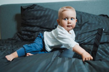 Küçük çocuk dizüstü bilgisayar kullanıyor, evde video izliyor, erken eğitim alıyor ve öğreniyor. Küçük çocuk dizüstü bilgisayara bakıyor ve yatakta otururken müzik dinliyor..