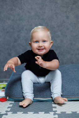 Mavi gözlü sarışın çocuk, 2 yaşında evde oynuyordu. Küçük çocuk kameraya bakıp gülümsüyor. Çocuklar için ev kıyafetleri.