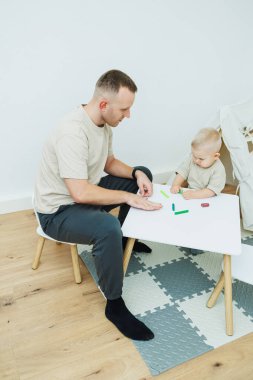 Babam 1.6 yaşındaki oğluna plastikten heykel yapmayı öğretiyor. Küçük çocuk babasıyla birlikte çocuk masasında oturur ve eğlenceli oyunlar oynar. Çocuk plastikten figürler yapıyor.