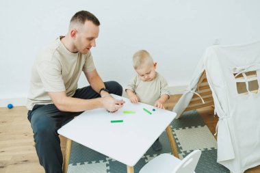 Babam 1.6 yaşındaki oğluna plastikten heykel yapmayı öğretiyor. Küçük çocuk babasıyla birlikte çocuk masasında oturur ve eğlenceli oyunlar oynar. Çocuk plastikten figürler yapıyor.
