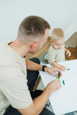 Babam 1.6 yaşındaki oğluna plastikten heykel yapmayı öğretiyor. Küçük çocuk babasıyla birlikte çocuk masasında oturur ve eğlenceli oyunlar oynar. Çocuk plastikten figürler yapıyor.