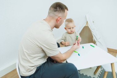 Babam 1.6 yaşındaki oğluna plastikten heykel yapmayı öğretiyor. Küçük çocuk babasıyla birlikte çocuk masasında oturur ve eğlenceli oyunlar oynar. Çocuk plastikten figürler yapıyor.