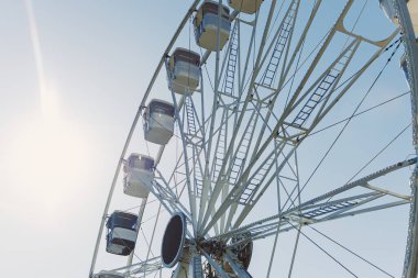 Mavi gökyüzüne karşı kamaraları olan büyük bir dönme dolap havalanıyor. Etrafı kapalı bir dönme dolap..