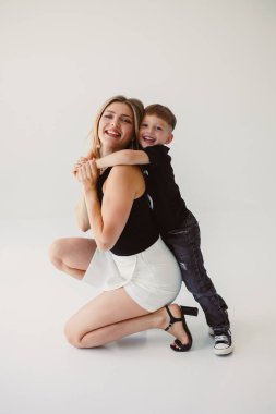 Anne ve 4 yaşındaki oğlu beyaz bir arka planda gülümsüyor ve sarılıyorlar. Anne ve oğul arasındaki sıcak ilişki. Anne ve oğul arasındaki aile ilişkileri kavramı.