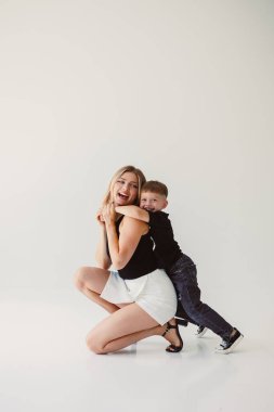 Beyaz arka planda otururken kucaklaşan tatlı anne ve bebek. Mutlu anne ve oğul, babalarının işten dönmesini bekliyorlar. Anne ve oğlunun eğlenceli oyunları..