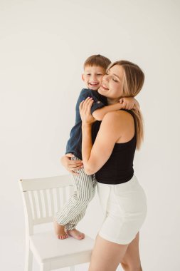 Beyaz arka planda otururken kucaklaşan tatlı anne ve bebek. Mutlu anne ve oğul, babalarının işten dönmesini bekliyorlar. Anne ve oğlunun eğlenceli oyunları..