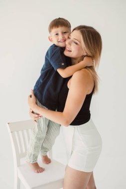 Beyaz arka planda otururken kucaklaşan tatlı anne ve bebek. Mutlu anne ve oğul, babalarının işten dönmesini bekliyorlar. Anne ve oğlunun eğlenceli oyunları..