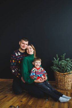 Neşeli bir aile portresi, sevgi dolu ebeveynler ve onların renkli Noel süveterleri içindeki sevimli çocuklarını içerir. Tatil sezonunda birlikte olmanın sıcak ruhunu yakalar.