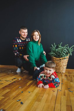 Yürek ısıtan bir aile portresi, renkli tatil kazakları içinde sevgi dolu ebeveynleri olan neşeli bir çocuğun evinde sıcak bir kutlamanın atmosferini yakaladığını gösteriyor.