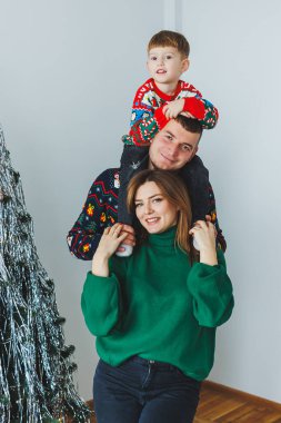 Güzel bir aile, Noel mevsiminin sıcağını neşeyle yakalıyor. Neşeli bir çocuk, babasının omuzlarına tünemiş, hepsi de Noel süsleriyle çevrili.