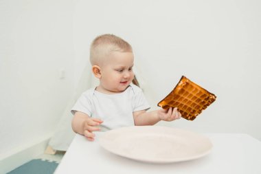 Çekici bir çocuk, basit bir masada oturan lezzetli bir altın waffle 'dan büyülenir. Parlak zemin, çocukların zevkini ve yiyecek merakını arttırır.