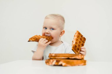 Neşeli bir çocuk renkli bir masada waffle 'dan zevk alır, yemek sırasında çocukluk ve aile birlikteliğinin neşesini gösterir, yemek yerken paylaşılan özel anların altını çizer