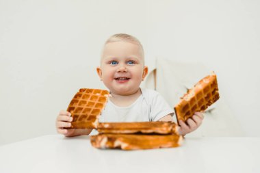 Neşeli bir bebek güzel dekore edilmiş bir masada oturur, iki çıtır waffle 'ı neşeyle tutar, çocukluk anılarının neşesini ve masumiyetini yakalar.