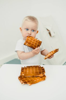 Neşeli ve mutlu bir çocuk, neşeli ve minimalist bir mutfak alanında saf neşeyle dolu neşeli ve iç açıcı bir anı gösteren lezzetli waffle 'lardan zevk alır.