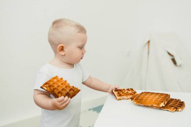 Kahvaltının aromalarıyla dolu parlak bir mutfakta neşeli bir çocuk iki waffle 'ı zevkle tutar ve eğlenceli çocukluklarında değerli bir merak anı yaratır.