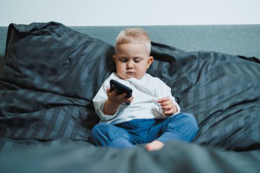 Renkli bir iç mekan ortamında, sevimli bir çocuk rahat bir kanepeye oturur, akıllı telefonlarına dalmış, merakı ve masumiyeti yayar ve içeriği keşfeder.