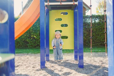 Neşeli bir çocuk neşeli bir oyun bahçesinde güneşli bir gökyüzünün altında durur. Etrafı renkli yapılarla çevrilidir. Çocukluk sevinci ve maceranın özünü somutlaştırır.