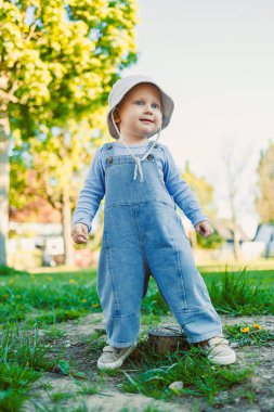 Canlı bir parkta, kot pantolon ve güneşli bir şapka giyen neşeli bir çocuk, çocukluğun masumiyetini ve açık hava keşiflerinin neşesini somutlaştırarak enerjik bir şekilde oynar.