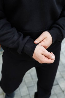 Bu yakın çekim görüntüsünde, parlak siyah bir kazağın manşetini dikkatlice ayarlayan elleri görüyoruz, gündelik moda ve modern stil kıyafetlerin özünü güzel bir şekilde vurguluyor.