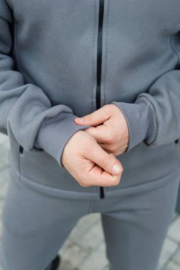 Modern atletizm eğilimlerini mükemmel bir şekilde gözler önüne seren ve ilgi çekici, aktif bir yaşam tarzını teşvik eden, modaya uygun gri eşofman ceketini dikkatlice ayarlayan ellerin yakın çekimi.