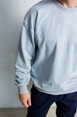 Bu yakın çekim, modaya uygun donanma pantolonu ile uyumlu, modern moda estetiğini vurgulayan, kapalı mekanda minimalist bir şekilde hazırlanmış şık, gri bir sweatshirt içeriyor.