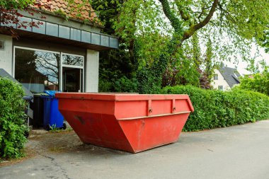 Büyük bir çöp konteynırı. İnşaat atığı için metal kırmızı konteynır. Tadilat sırasında evin yanında duran çöp konteynırı..