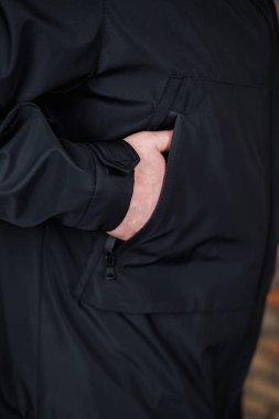 Görüntü, modern moda eğilimlerini vurgulayan ve rahatlık duygusunu vurgulayan modaya uygun bir siyah ceketin cebinde gelişigüzel dinlenen bir elin yakın çekimini net bir şekilde gösteriyor.