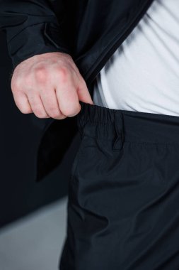 Bir erkek zarif siyah atletik pantolonunun çizgili ipini ustalıkla ayarlar, modern aktivite kıyafetinin karakteristik özellikleri olan konfor ve stilin mükemmel bir karışımını sergiler.