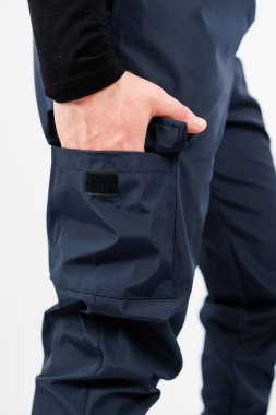 Görüntü, bir elin şık lacivert kargo pantolonuna uzanarak, onların açık hava aktiviteleri ve şehir kıyafetleri için pratik ve modasını ön plana çıkardığını gösteriyor.