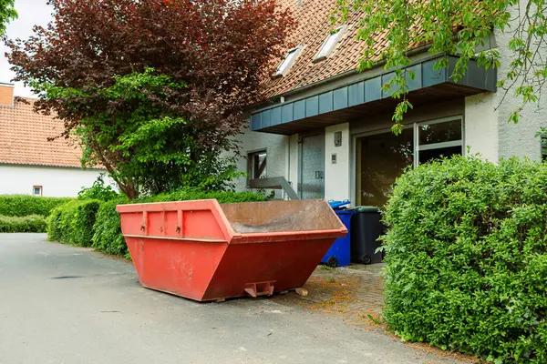 Büyük bir çöp konteynırı. İnşaat atığı için metal kırmızı konteynır. Tadilat sırasında evin yanında duran çöp konteynırı..