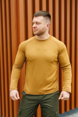 Kendine güvenen bir adam, çağdaş bir arkaplanda rahatça duran, uzun kollu hardal gömleği ve yeşil pantolonu sergiliyor. Moda ve yaşam tarzı temaları için mükemmel.