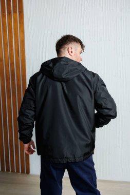 Şık bir erkek model, şık, siyah kapüşonlu bir ceket giyiyor. Arkasından zarif bir şekilde çekilmiş. Modern modanın özünü güzel ve şık bir ahşap zemine karşı sergiliyor.