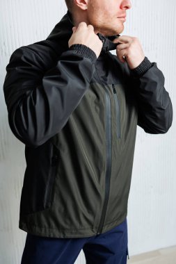 Modaya uygun bir adam modaya uygun fermuarlı kapüşonlu ceketini düzeltir, gösterişli, minimalist bir ortamda çağdaş açık hava kıyafetlerini sergiler, şık havasını yükseltir.