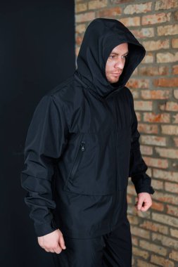 Bir erkek manken, çağdaş bir şehir arkaplanına karşı şık, siyah kapüşonlu bir ceket sergiliyor. Hem moda hem de açık hava fotoğrafçılığı için cazibesini vurguluyor.