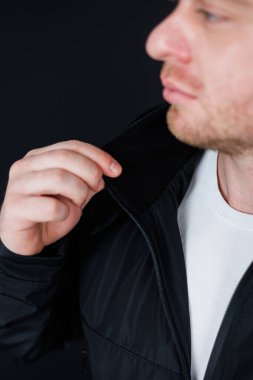 Modaya uygun bir adam siyah ceketinin yakasını düzeltirken görülüyor. Koyu bir arka plana karşı şık bir görünüm sergiliyor. Moda içeriği için mükemmel.