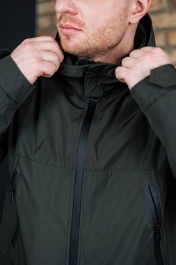 Şık bir adam kapüşonlu ceketini düzeltirken, hem şehir yaşamı hem de heyecan verici açık hava maceraları için ideal çağdaş açık hava modasını sergilerken görülüyor.