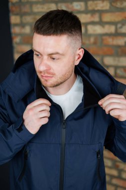 Şık bir donanma ceketi giyen kendine güveni olan bir adam, ideal bir yaşam tarzı fotoğrafçılık ortamında belirgin kişiliğini sergileyen, dokulu tuğla bir duvara karşı zahmetsizce poz verir.