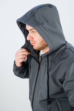 Estetik açıdan minimalist bir ortamda, genç bir adam, şehir modasının en son modelini sergileyen modaya uygun bir kapüşonlu giyiyor.