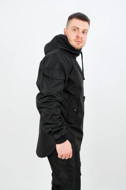 Tarz sahibi genç bir adam siyah atletik bir ceketle sade bir arka plana karşı durarak modern şehir modası için mükemmel bir görünüm sergiliyor..