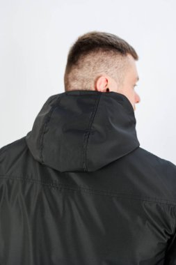 Gösterişli siyah kapüşonlu ceket giyen şık bir genç adam, arkasında mükemmel bir şekilde çeşitli çağdaş şehir moda tarzları ve heyecan verici giyim terfileri sergiliyor.
