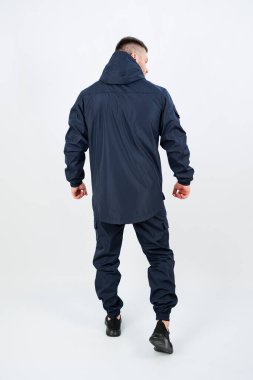 Bir adam kendine güvenen koyu mavi bir açık hava elbisesi içinde duruyor. İçinde şık bir kapüşonlu ceket ve eşleşen pantolon var. Doğadaki her türlü maceraya uygun.
