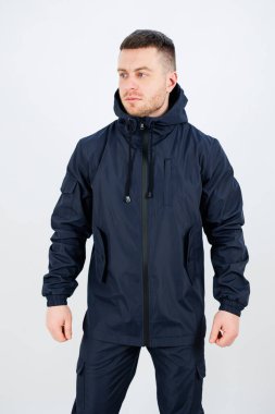 Kapüşonlu lacivert su geçirmez ceket giyen şık bir adam. Açık hava aktiviteleri ve günlük giysiler için mükemmel. Moda ve işlevsellik arayan moda belirleyiciler için ideal.