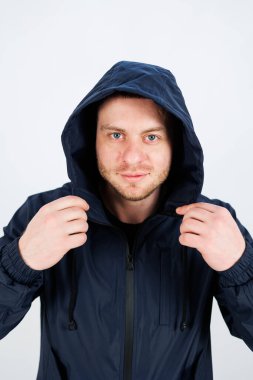 Genç bir adam, şık, koyu renk kapüşonlu ceketini düzeltirken özgüvenle gülümsüyor. Bu da onu çeşitli yaşam tarzı temaları ve moda içeriği için mükemmel bir seçim yapıyor.