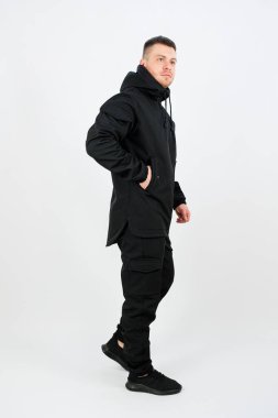 Şık bir şehirli adam, gösterişli ve zahmetsizce, gösterişli siyah bir elbise içinde, temiz ve minimalist beyaz bir arka plana karşı modern sokak giyimi tarzını sergiliyor.