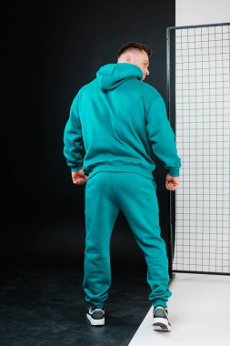 Modern bir stüdyoda, formda bir erkek model aktif yaşam tarzları ve fitness meraklıları için konfor ve tarzın karışımını vurgulayan, modaya uygun deniz mavisi kıyafetleri sergiliyor.