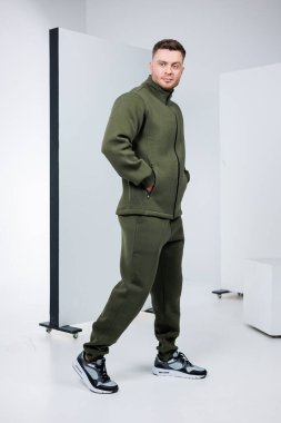 Şık ve modaya uygun bir erkek model modern çağdaş bir stüdyo ortamında hem konfor hem de stili mükemmel bir şekilde birleştiren sıradan bir zeytin yeşili eşofman sergiliyor.