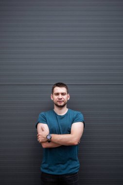 Kendine güvenen bir adam, kollarını şık bir mavi tişörtle modern yaşam tarzı ve moda temalarını sergilemek için mükemmel olan parlak gri bir arka plana karşı kenetlenir.
