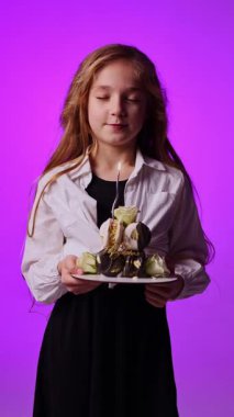 Doğum günü pastasında mum söndüren 8 yaşında tatlı bir kız. Ellerinde pasta tutan neşeli bir kız. Tatlı çocuğun doğum günü.